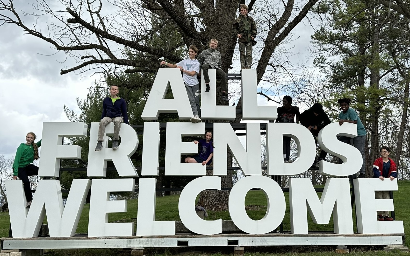 Children posing on large letters that spell "All Friends Welcome"