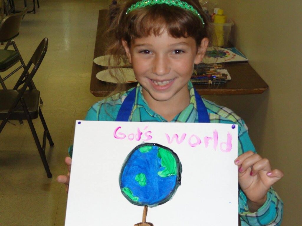 Student holds a panting showing the earth and the words, "God's World"