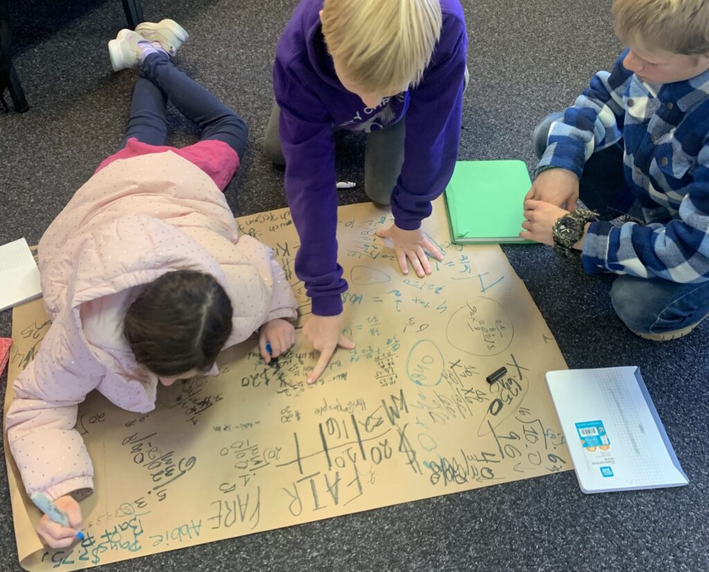 Three students sit together on the floor working on a math project